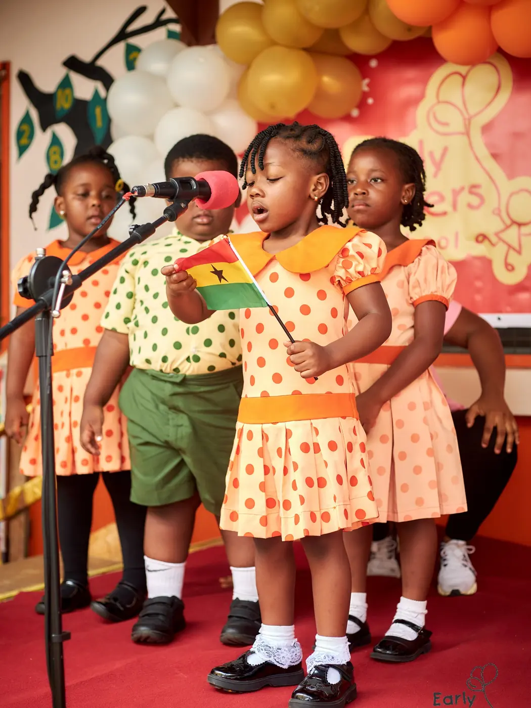 Children in orange polka-dot uniforms singing together