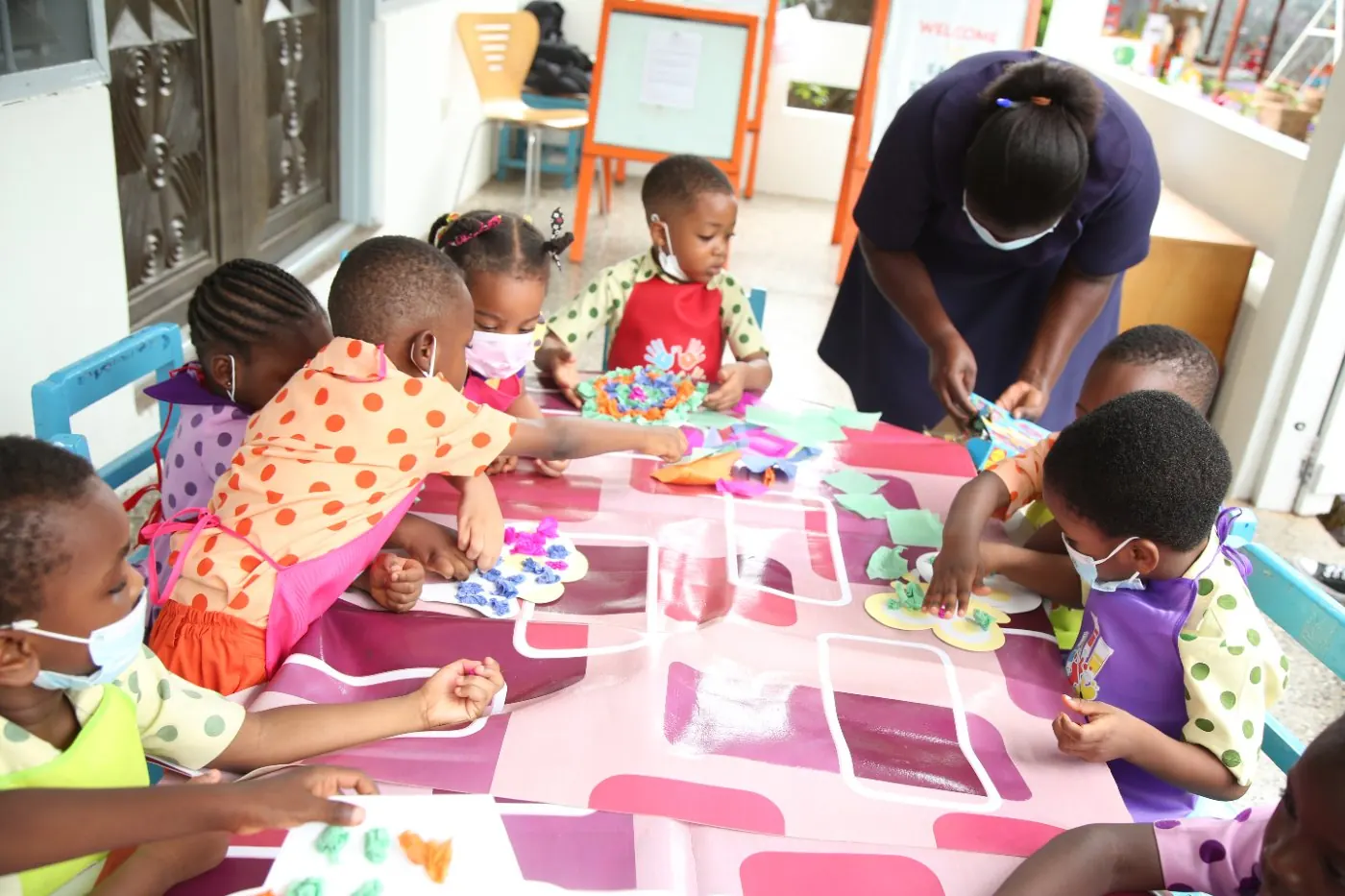 Children working together at a craft table with their teacher