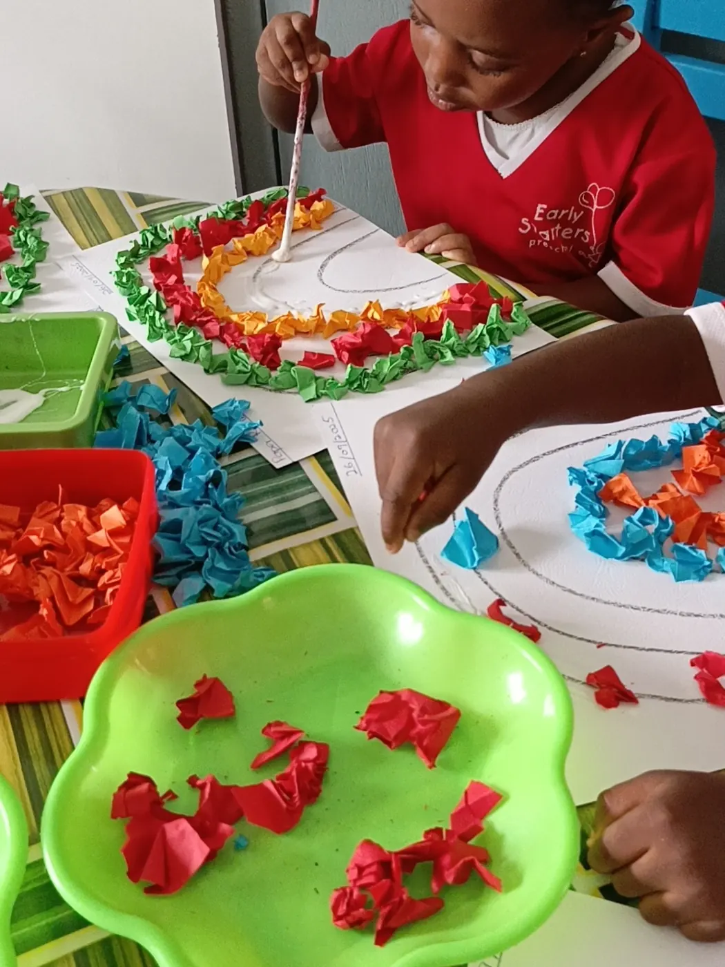 A child gluing crumpled tissue paper into a colourful picture