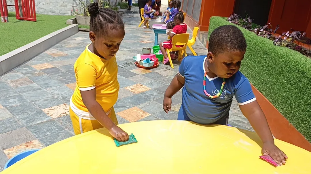 Two children wiping a table clean outdoors
